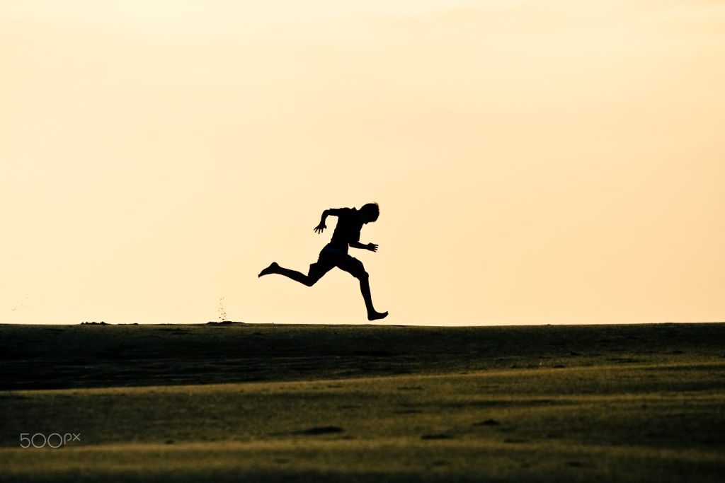 Silhouette of a runner mid-stride against an orange sky