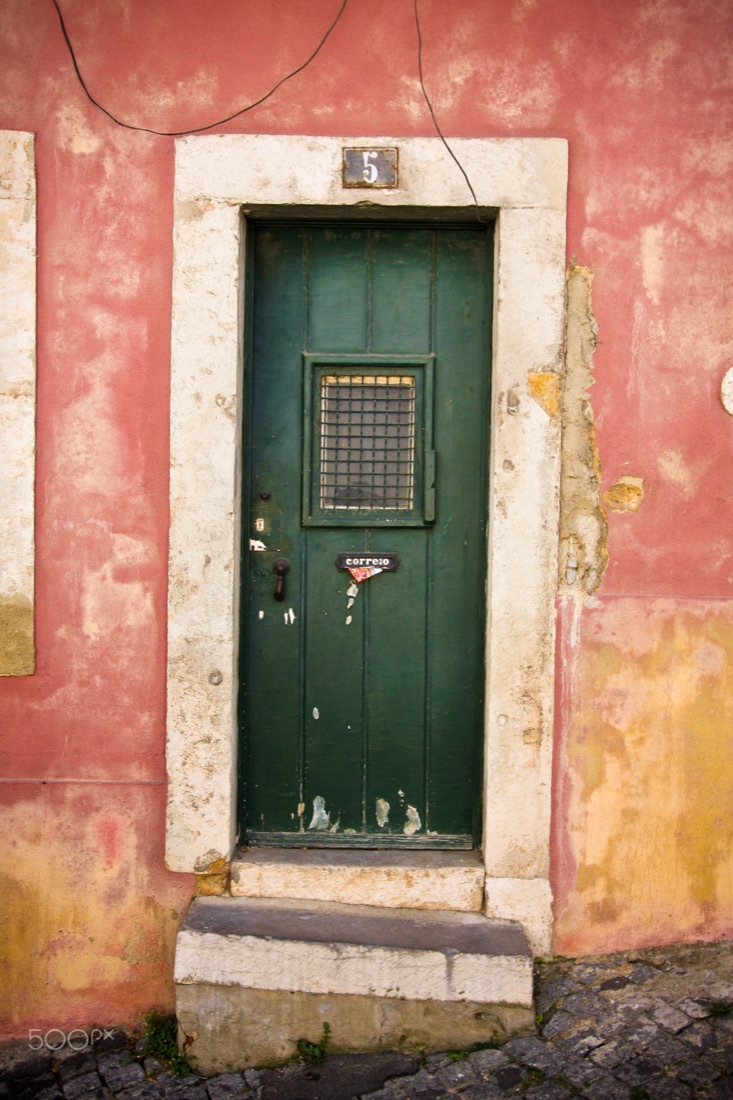 A green door numbered 5 in a weathered pink wall