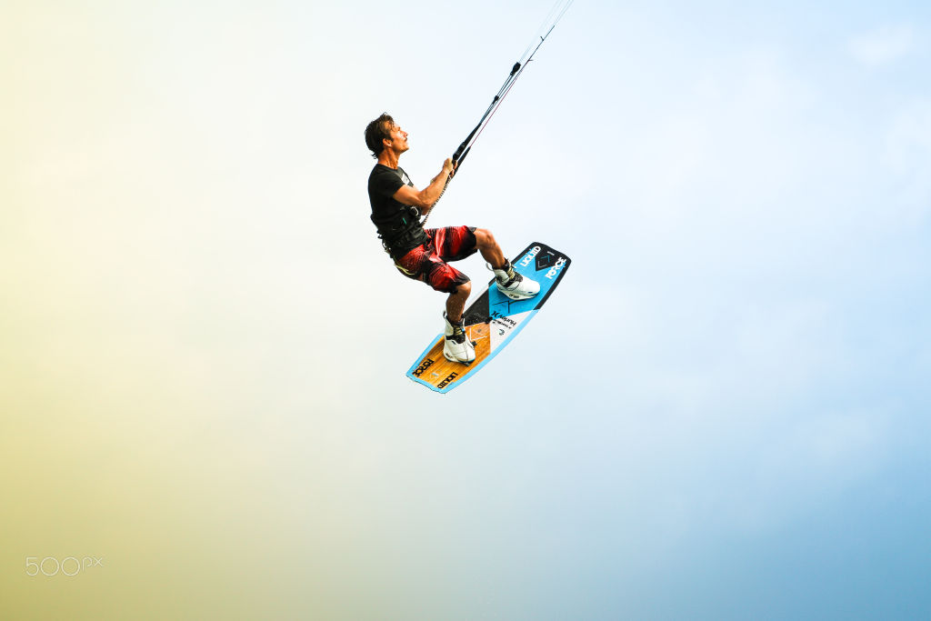 Kitesurfer mid-jump against a pale sky