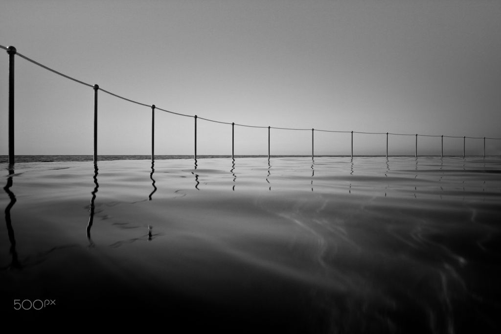 Black and white long exposure of a rope fence running into calm water