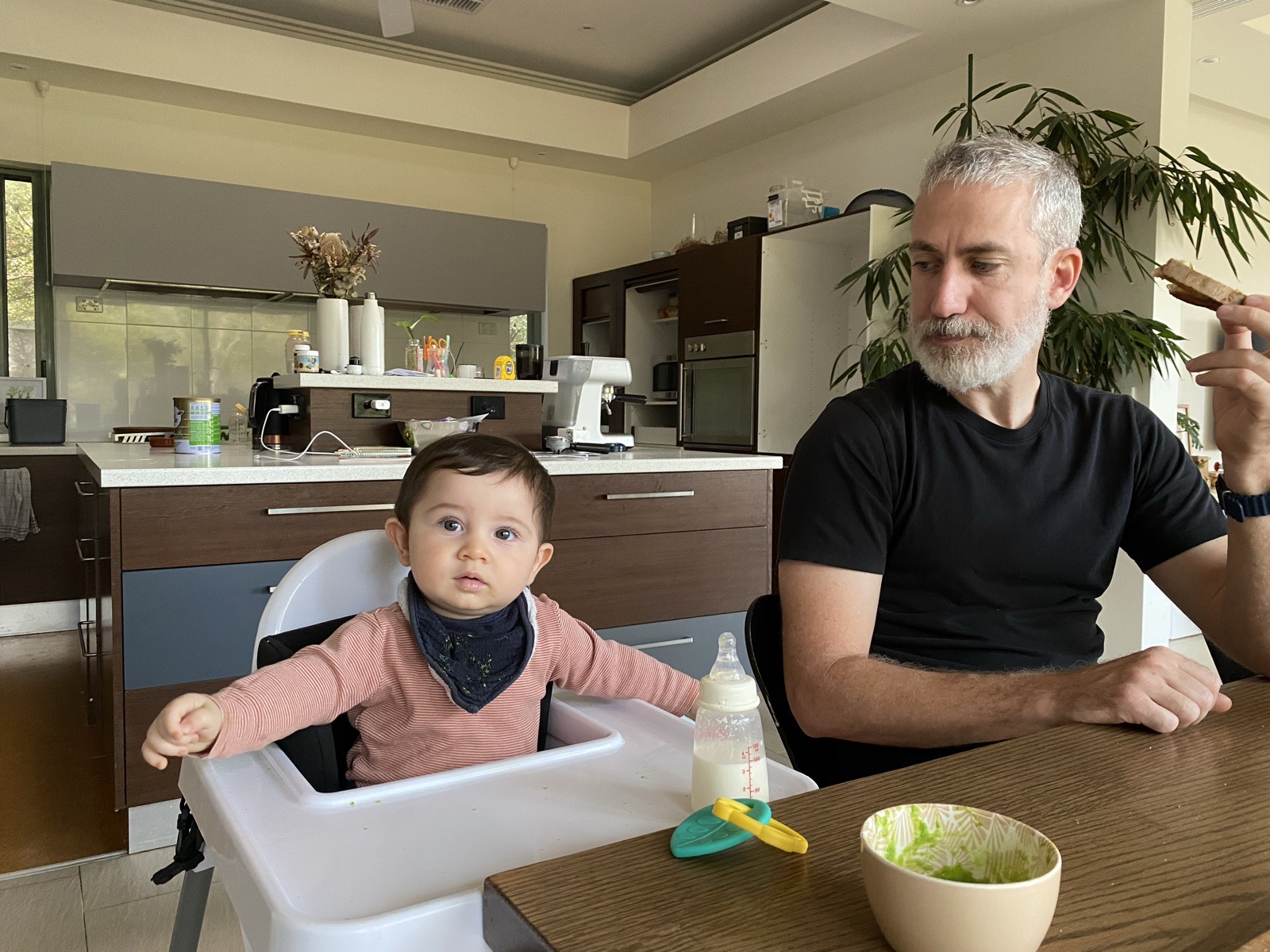 Breakfast at home: the baby in a high chair, Pierre alongside with a slice of toast