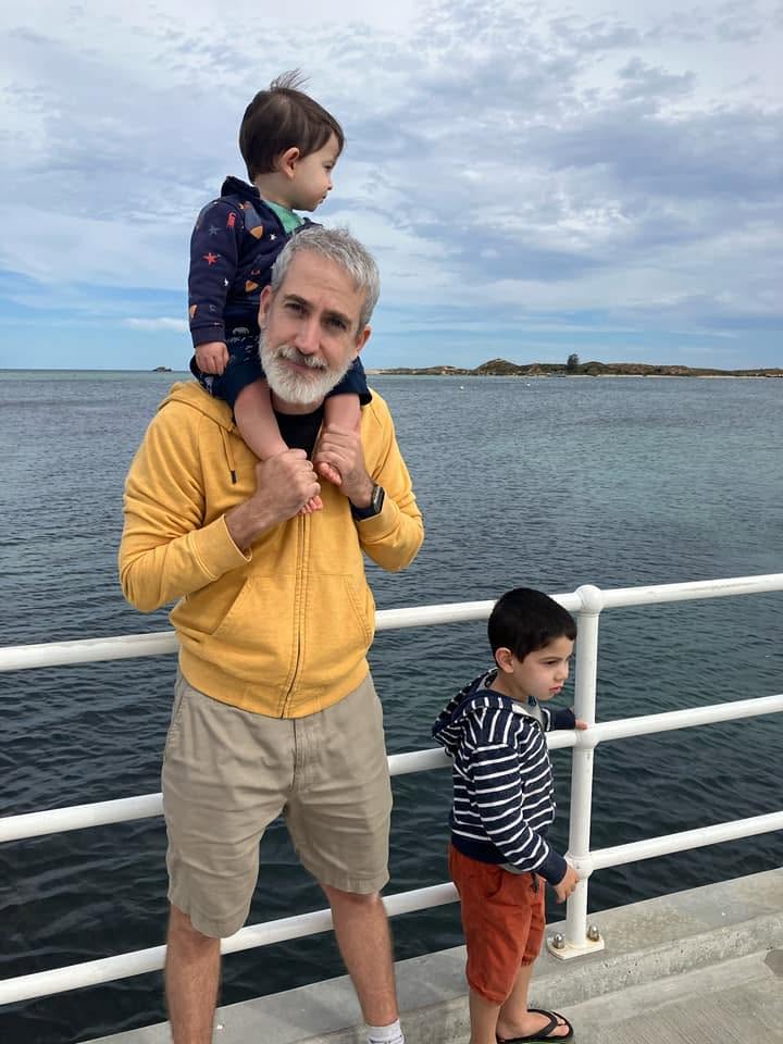 Pierre on a pier by the ocean with his two sons, the youngest on his shoulders